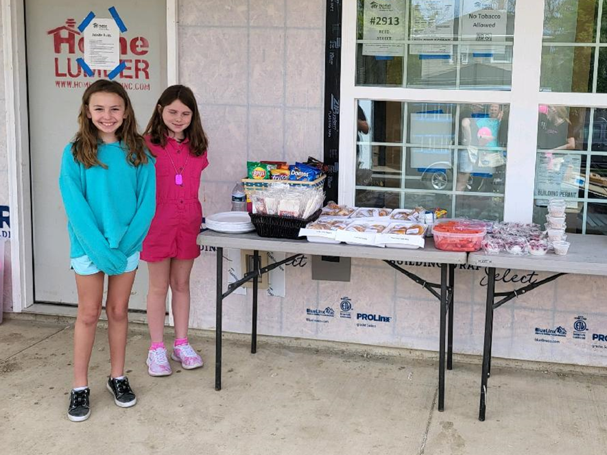 Two young girls standing near donated lunch on construction site